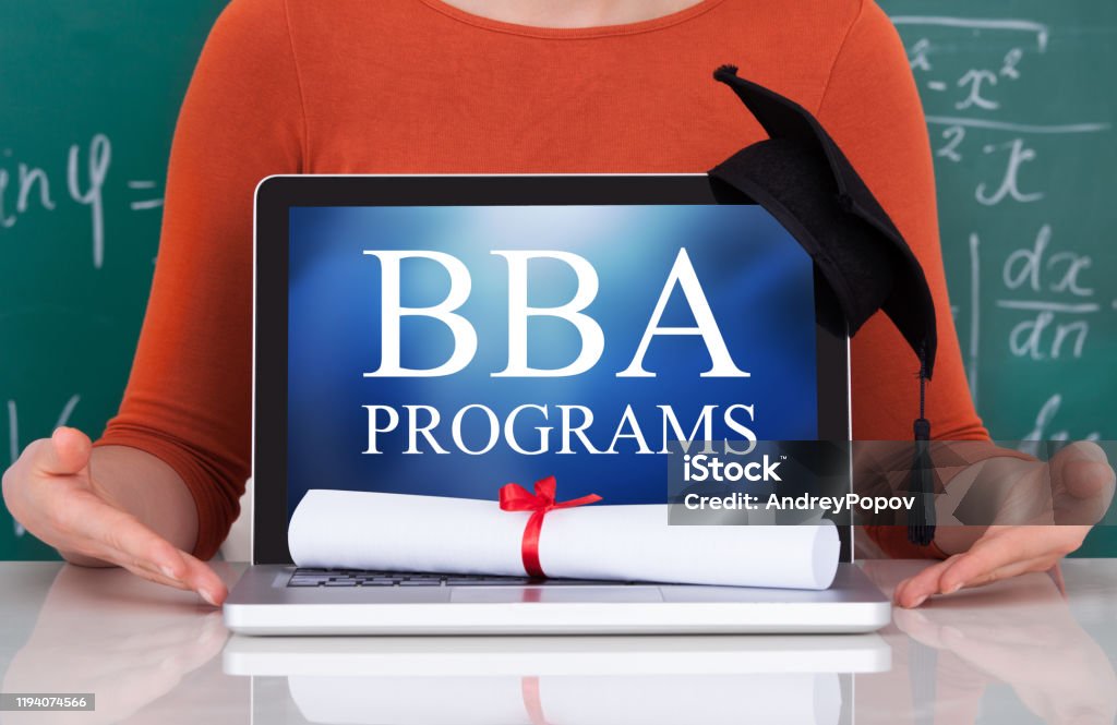 bba Midsection of young college student showing laptop with mortarboard and degree in classroom